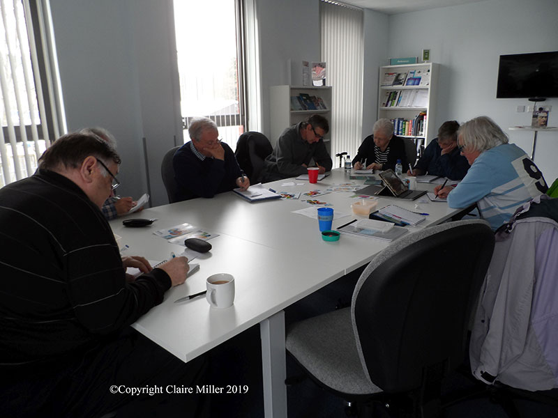 Photograph of people sitting around a table writing, in a writing workshop being run by Claire Miller Author.